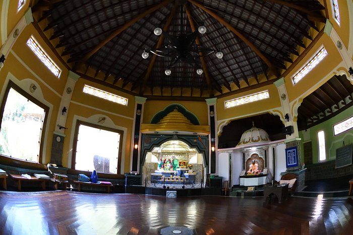 Interior do templo do Dharma Shala: teto de madeira em leque, paredes amarelas e altares ao fundo