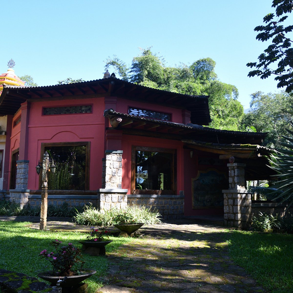 Fachada do pavilhão vermelho com colunas de pedra e jardim gramado